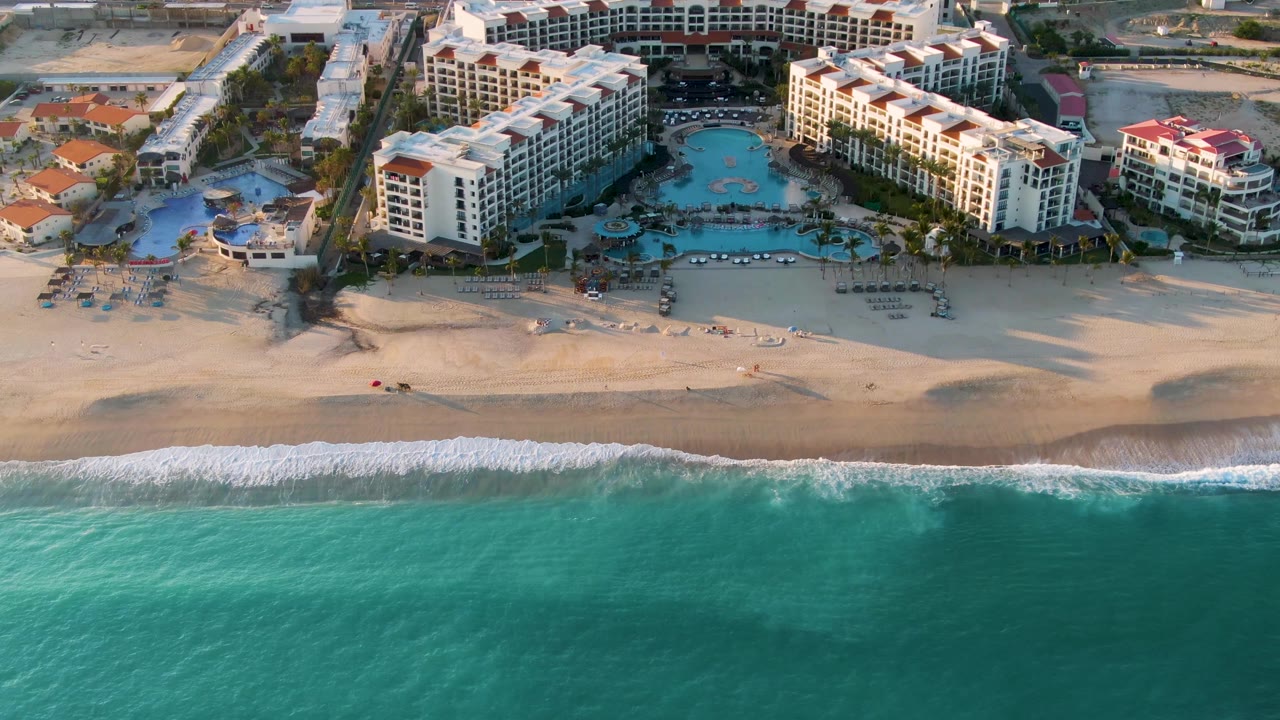 Aerial view of a beach resort, sandy shoreline, turquoise ocean, and pools.