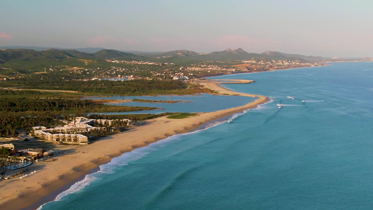 Aerial coastline with lagoon, beach resort buildings, and low waves