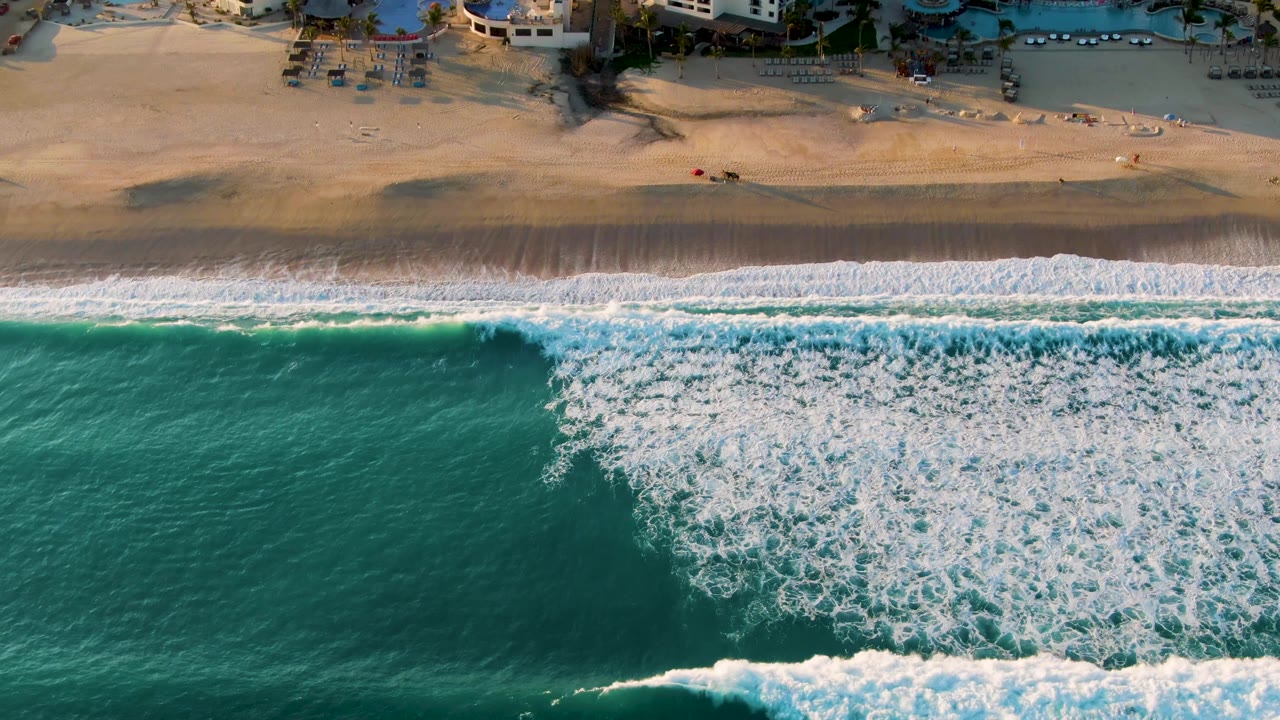 White surf spreads across turquoise water below a sandy shoreline.