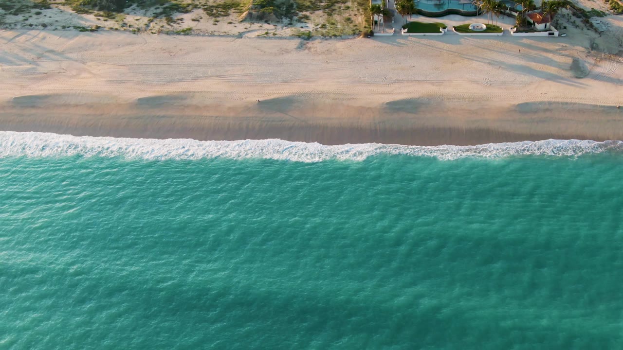 Overhead view of gentle surf reaching a pale sandy beach.