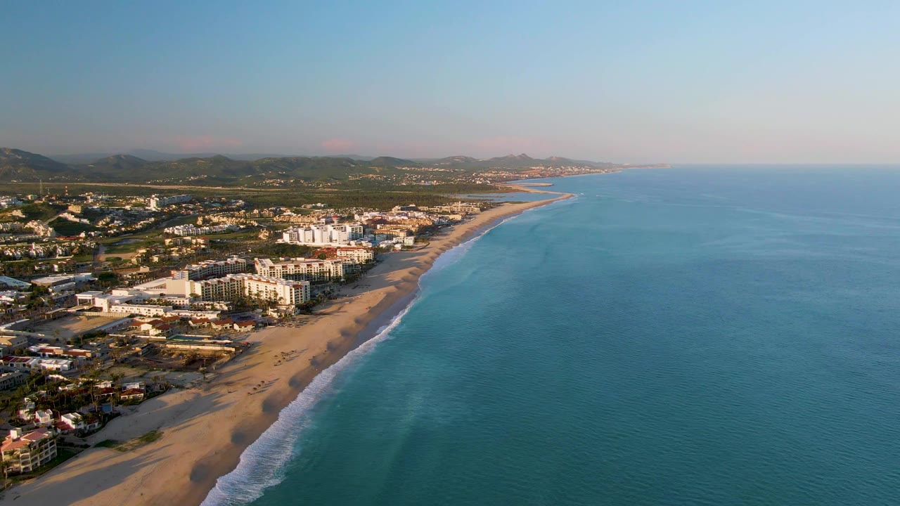 Beachfront buildings beside a curving sandy shoreline and calm ocean