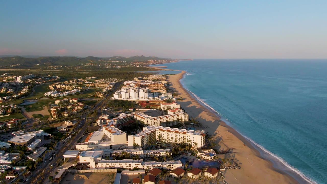 Aerial beach resort view with ocean waves and hills under dawn light.