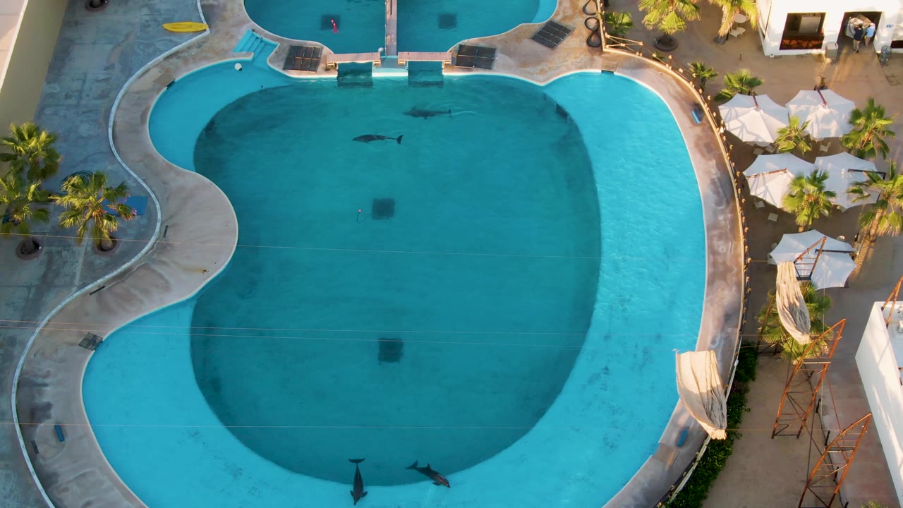 At two seconds, the overhead view shows swimmers farther apart in the San Jose Del Cabo hotel pool, with bright turquoise edges and a darker central water area.