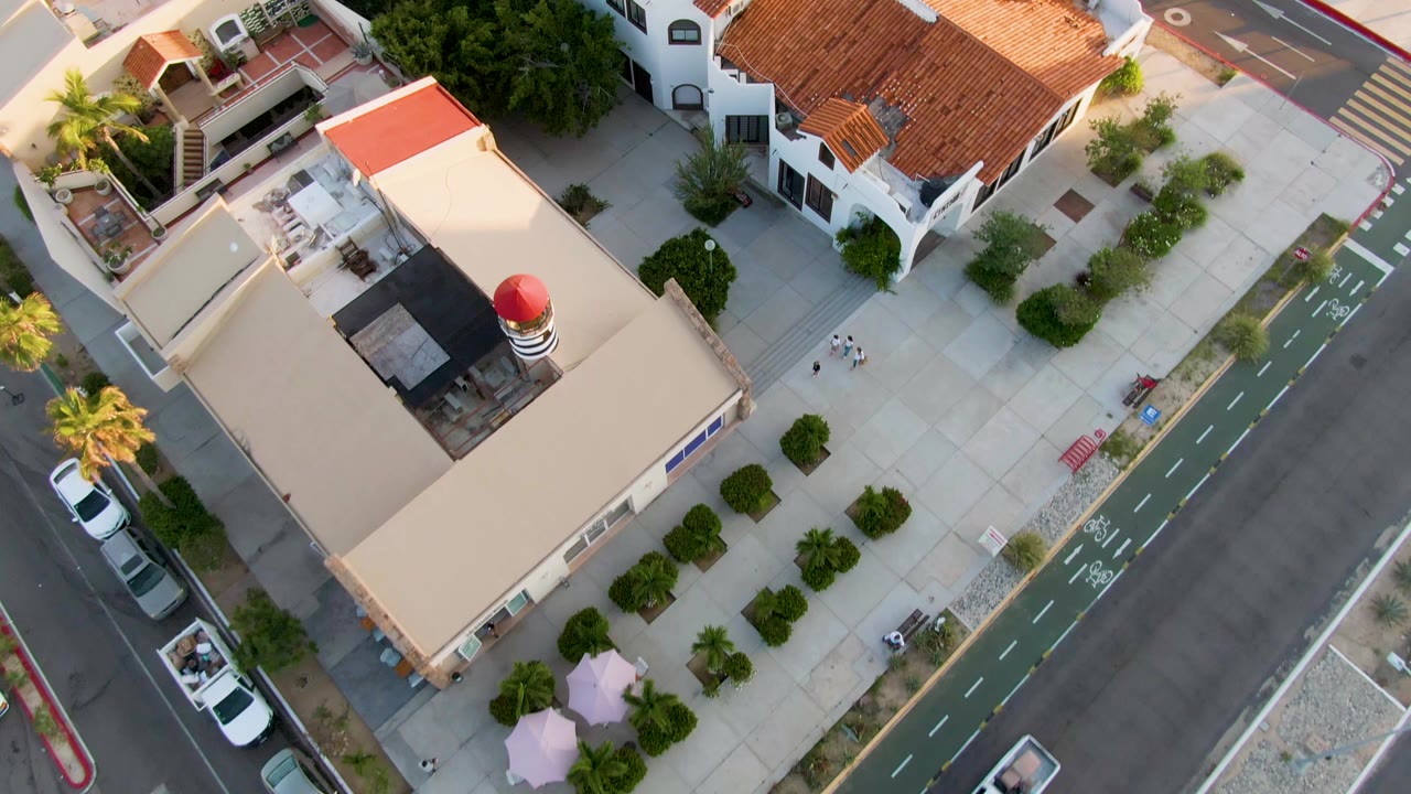 Aerial view of a tan building with a small red dome, sidewalk trees, street, bike lane, and parked cars.