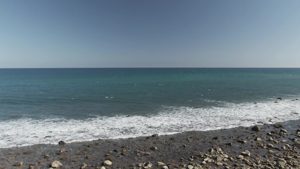 Ocean waves breaking over a rocky shoreline beneath a pale sky.
