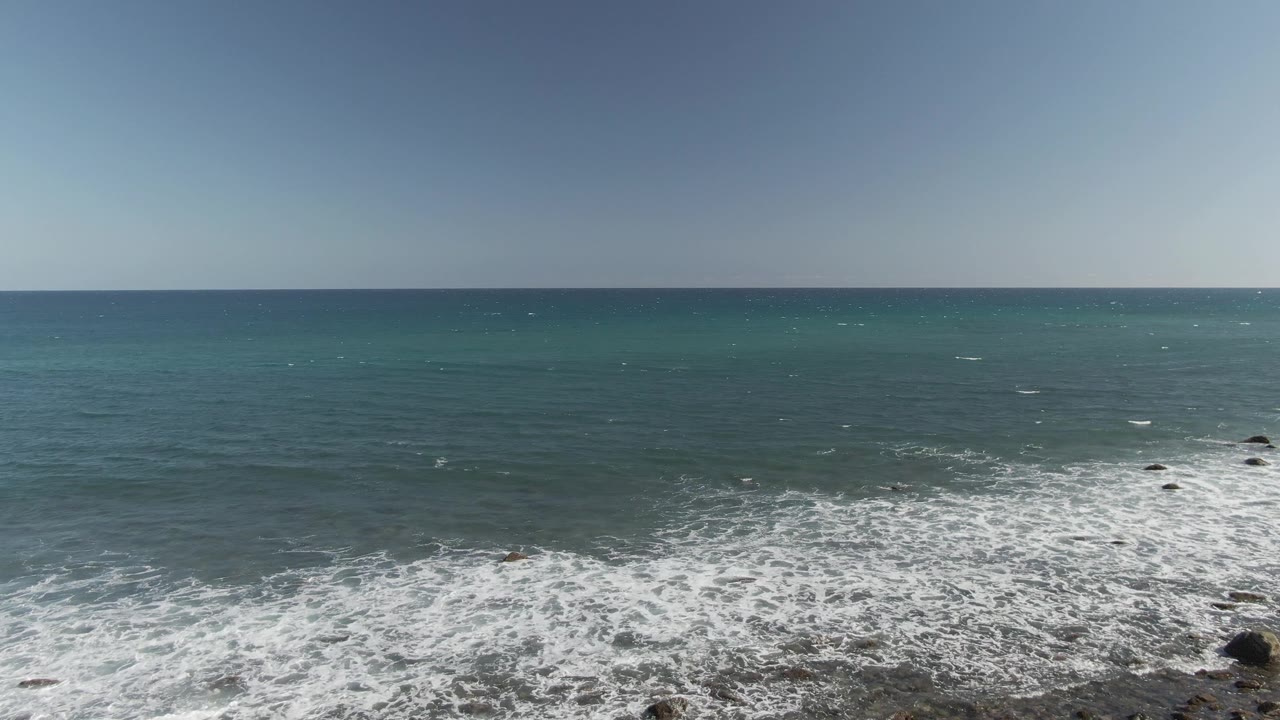 At Costa Azul Los Cabos, the foam line pushes across the lower right rocky foreground while small offshore rocks break the surface, with no visible people.