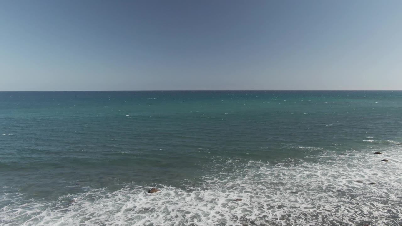 At Costa Azul Los Cabos, the surf sits lower in frame with more open blue-green water visible across the middle distance, and no visible people appear on the shore or water.