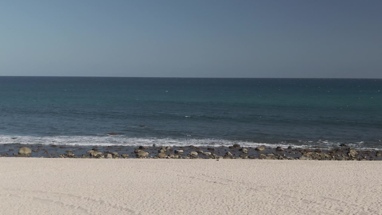White sand beach with ocean waves breaking behind a rocky shore.