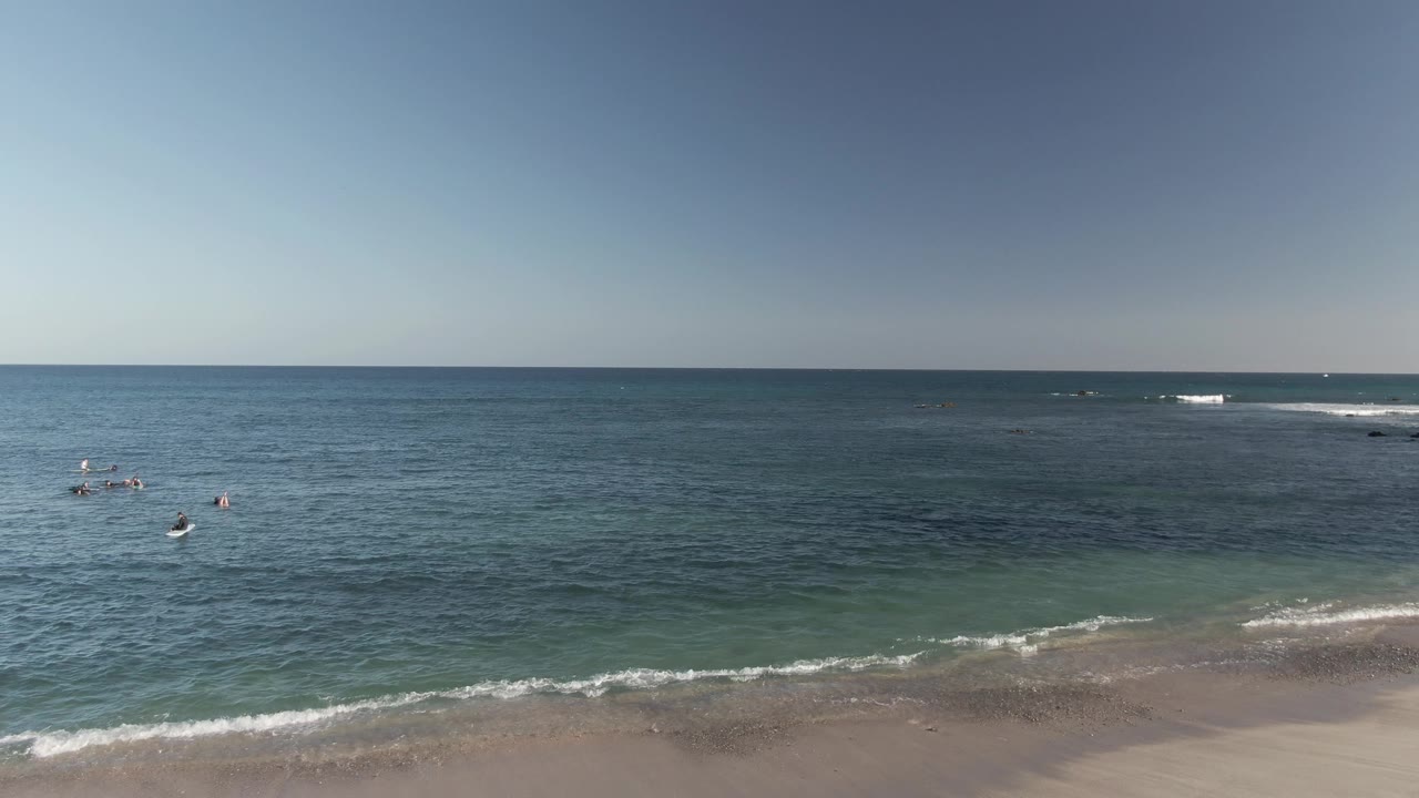 Sandy shoreline with ocean waves and distant swimmers