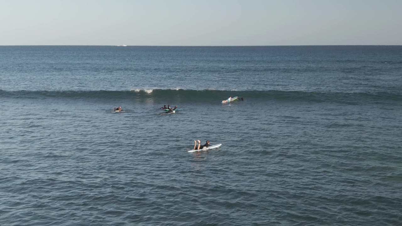Surfers spread across open water with a wave cresting behind them.