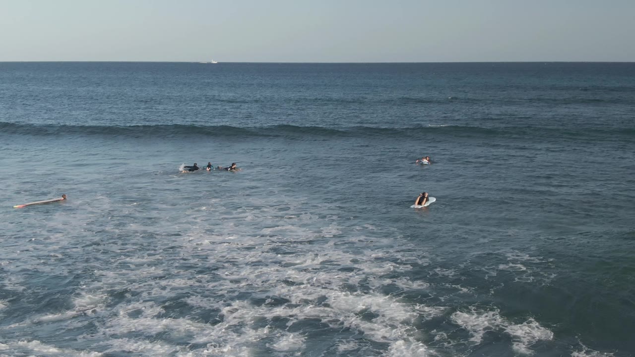 Surfers remain spread across the water while a dark wave line forms behind them.
