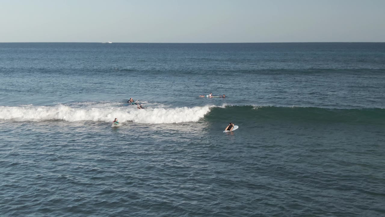 Aerial view at Costa Azul Los Cabos shows surfers and bodyboarders positioned along a white breaking wave with blue open water beyond.