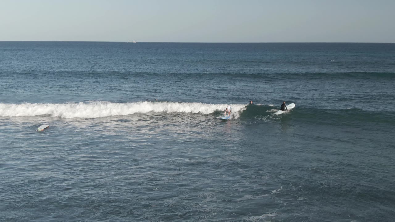 Several riders are visible along a long white breaking wave at Costa Azul Los Cabos, with open ocean in front and the horizon in the background.