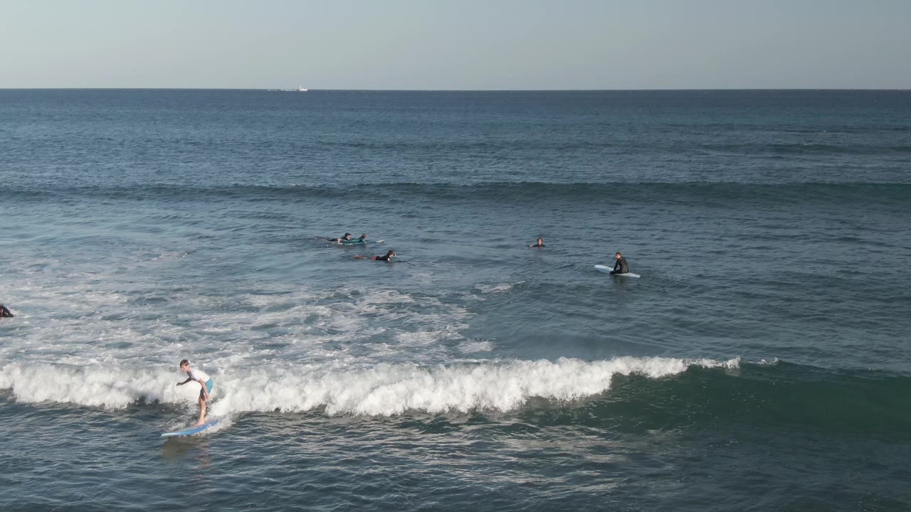 Surfer continues across whitewater as surfers wait beyond the break.