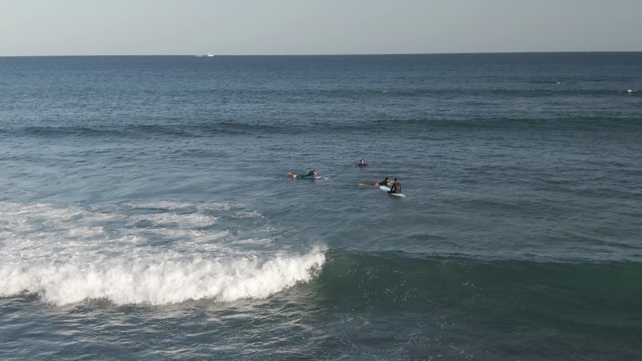Surfers on boards wait in the water as a wave breaks below them.