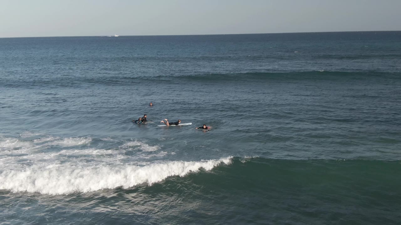 Small group of surfers floats near whitewater under a clear horizon.