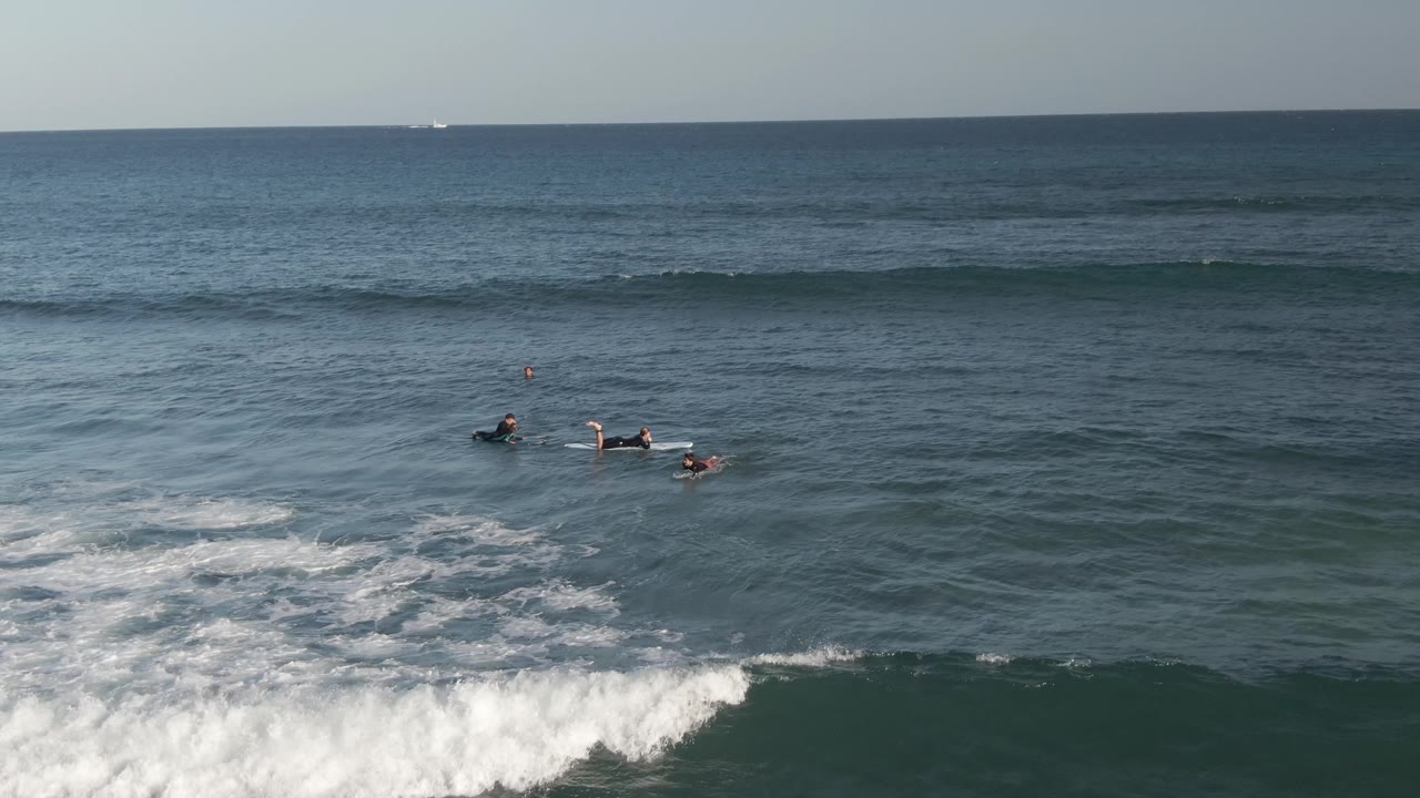 At Costa Azul Los Cabos, the surfers appear on the right side of the frame as a curling line of whitewater moves through the lower ocean surface.