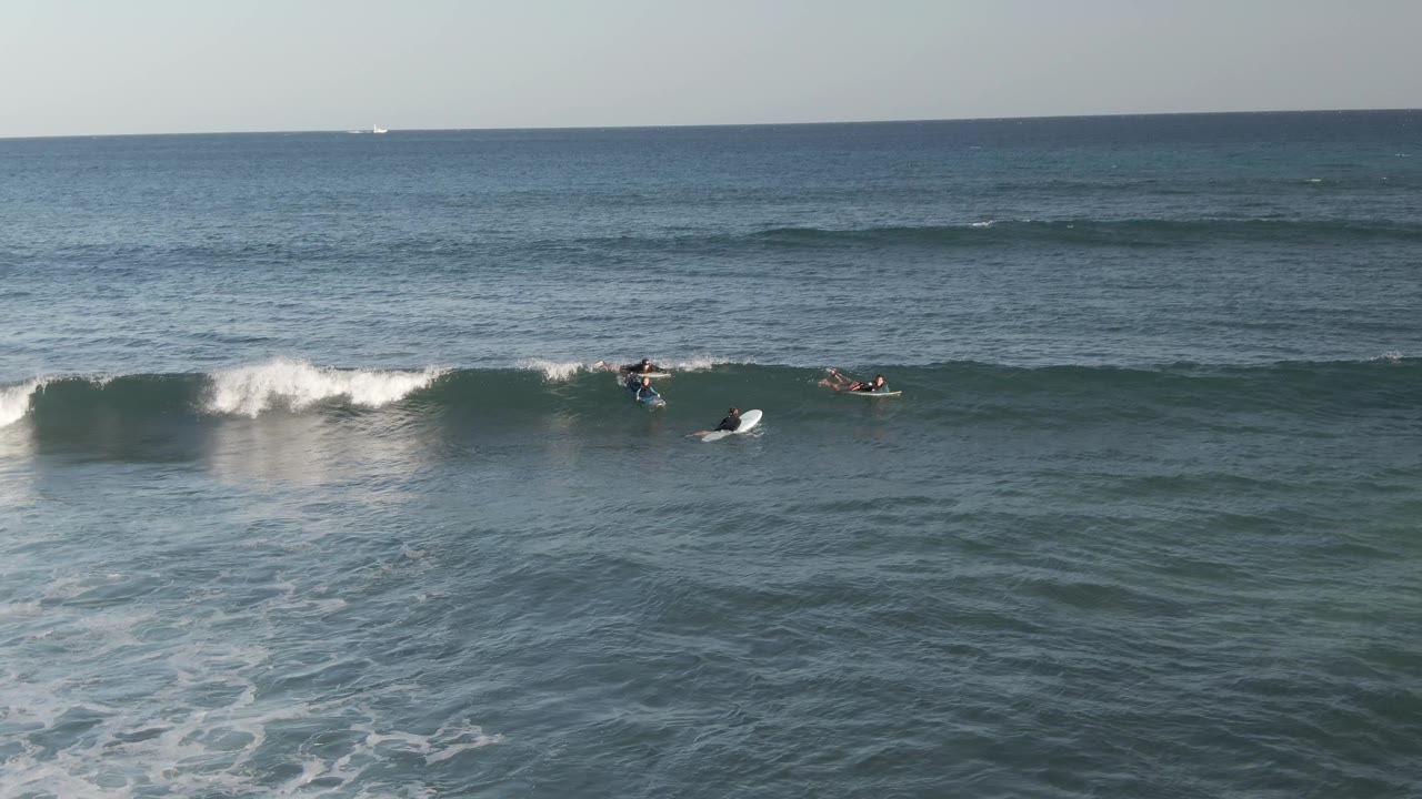 At Costa Azul Los Cabos, the wave has broken into whitewater across the right midground, with surfers and boards clustered near the shoulder.