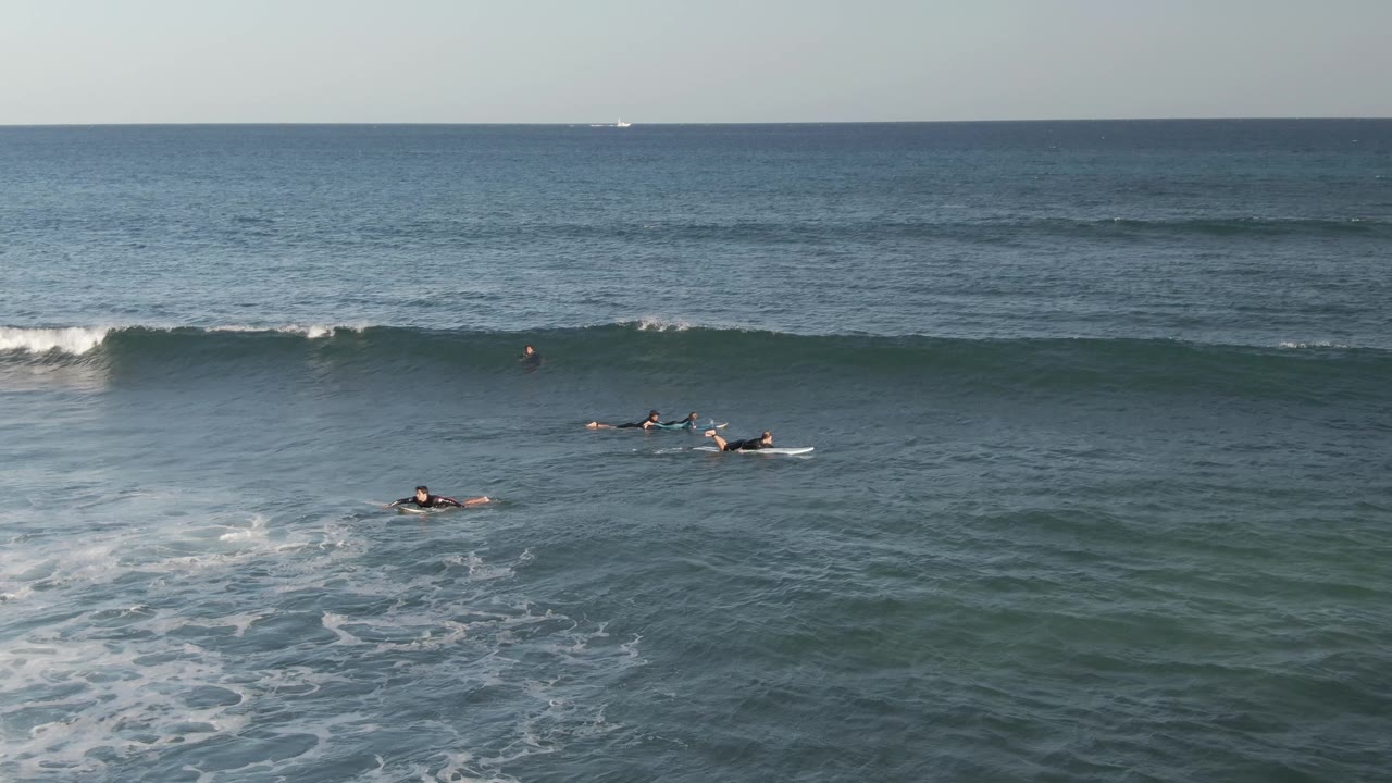 Small groups of surfers paddle near a dark wave line in open water.