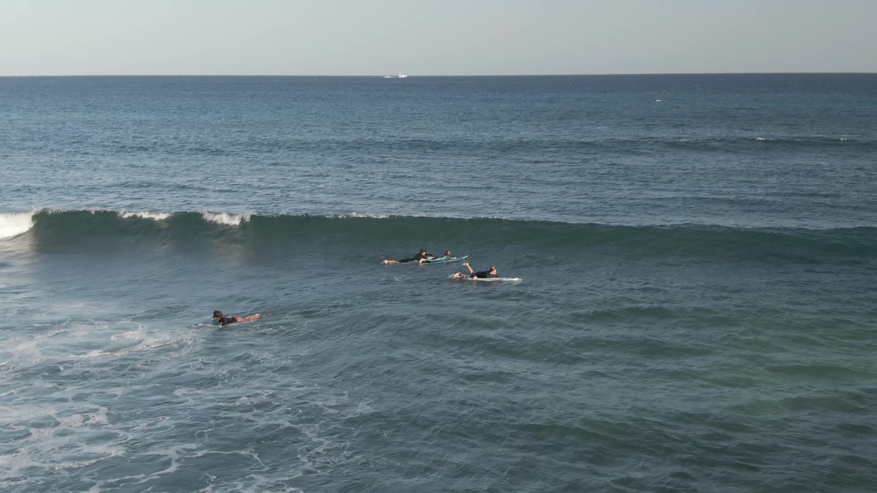 Surfers in the water at Costa Azul Los Cabos face a wave that is starting to break, with white spray on the right and open sea beyond the lineup.