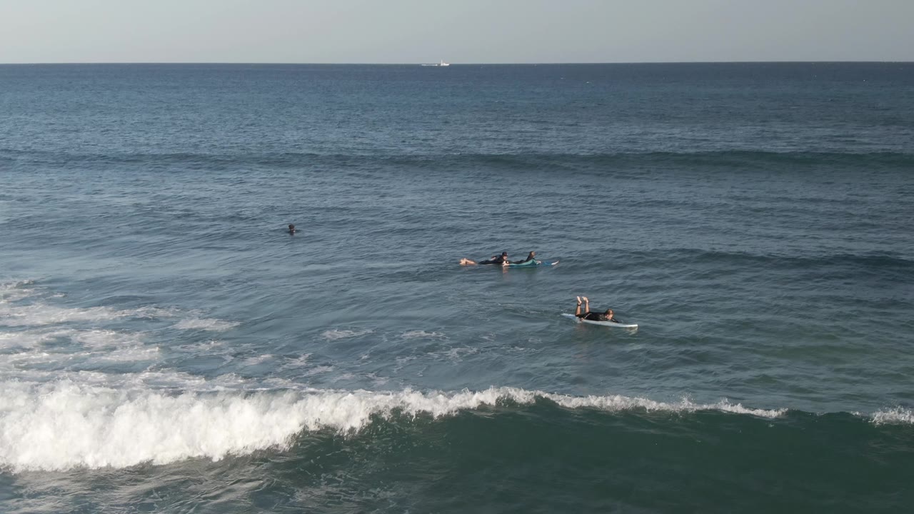 A foamy wave breaks across the midground in Costa Azul Los Cabos while distant surfers paddle and wait on either side of the whitewater.