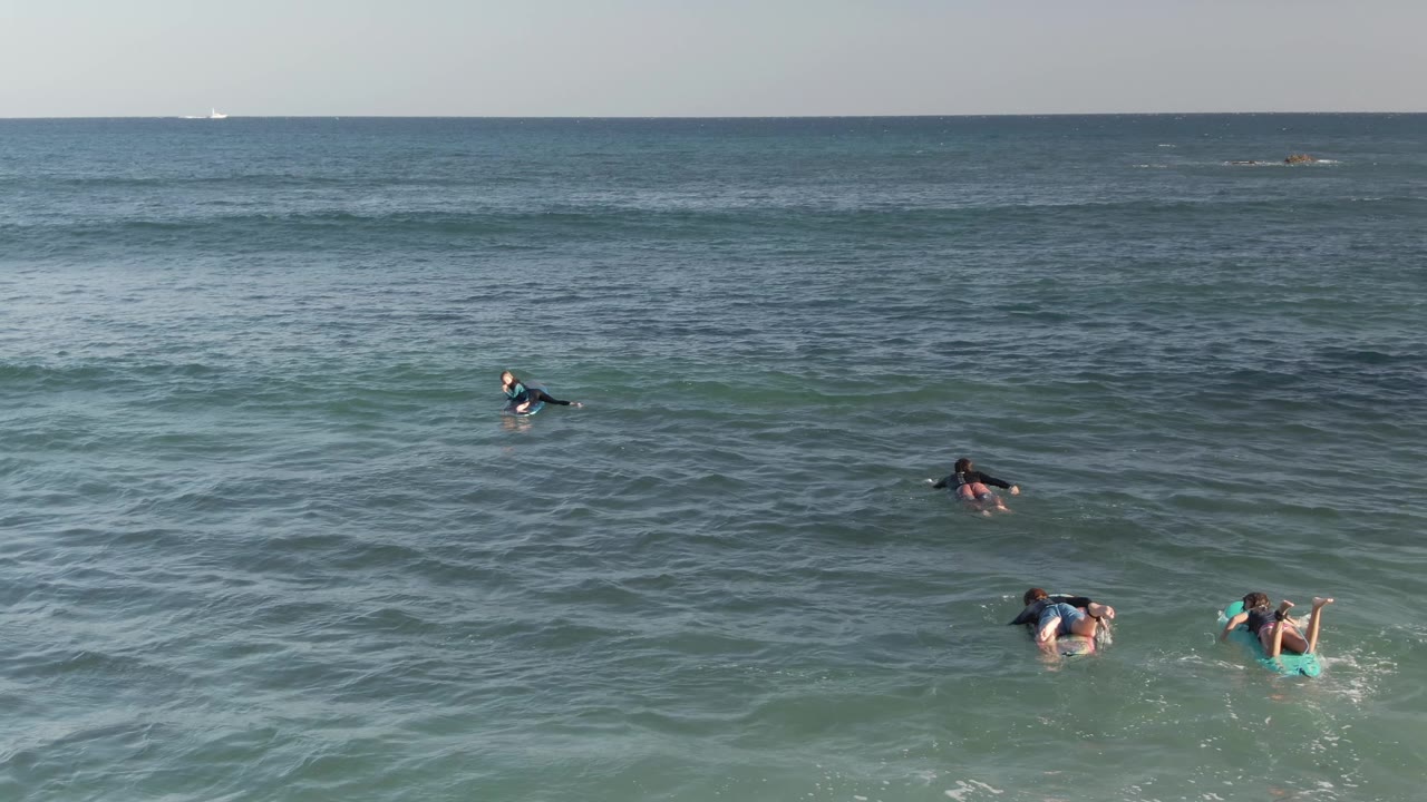 At Costa Azul Los Cabos, multiple people remain visible on boards as small waves pass through the midground and open sea fills the background.