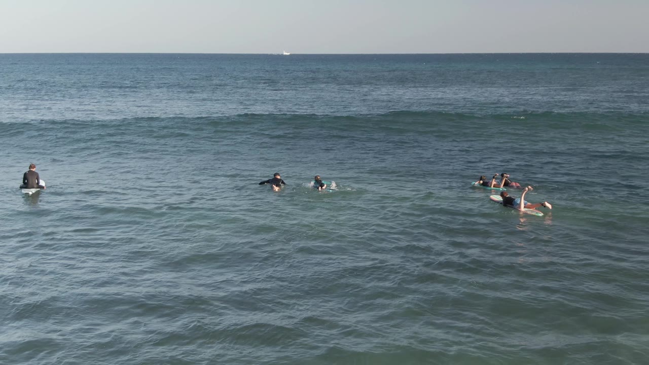 Surfers sit and paddle on boards in blue-green ocean water at Costa Azul Los Cabos, with the horizon high in the frame and people spread across the swell line.