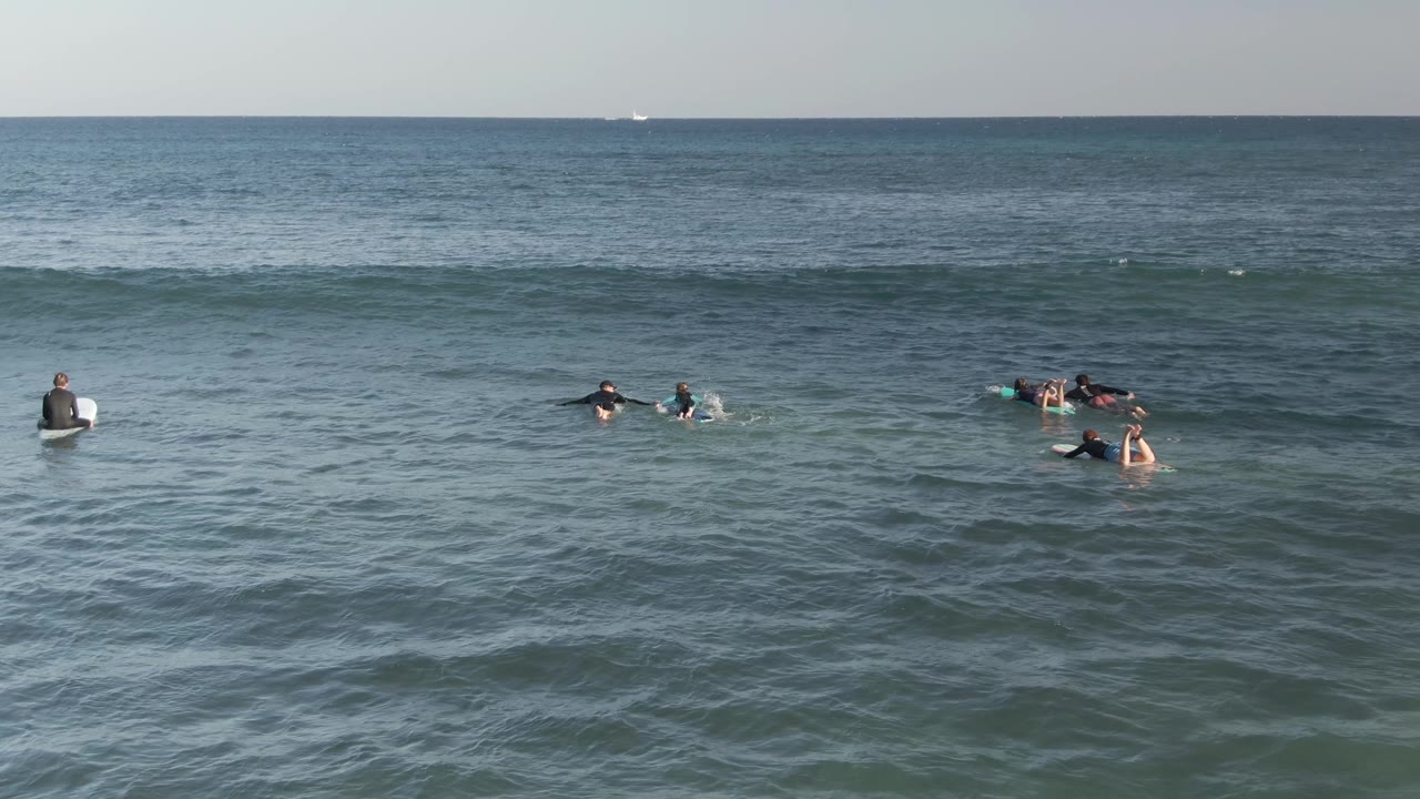 Small groups of surfers paddle and sit on surfboards in open water.