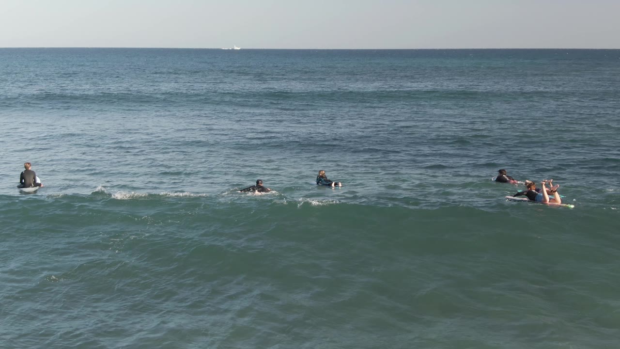Surfers paddling and sitting beyond a gentle wave.