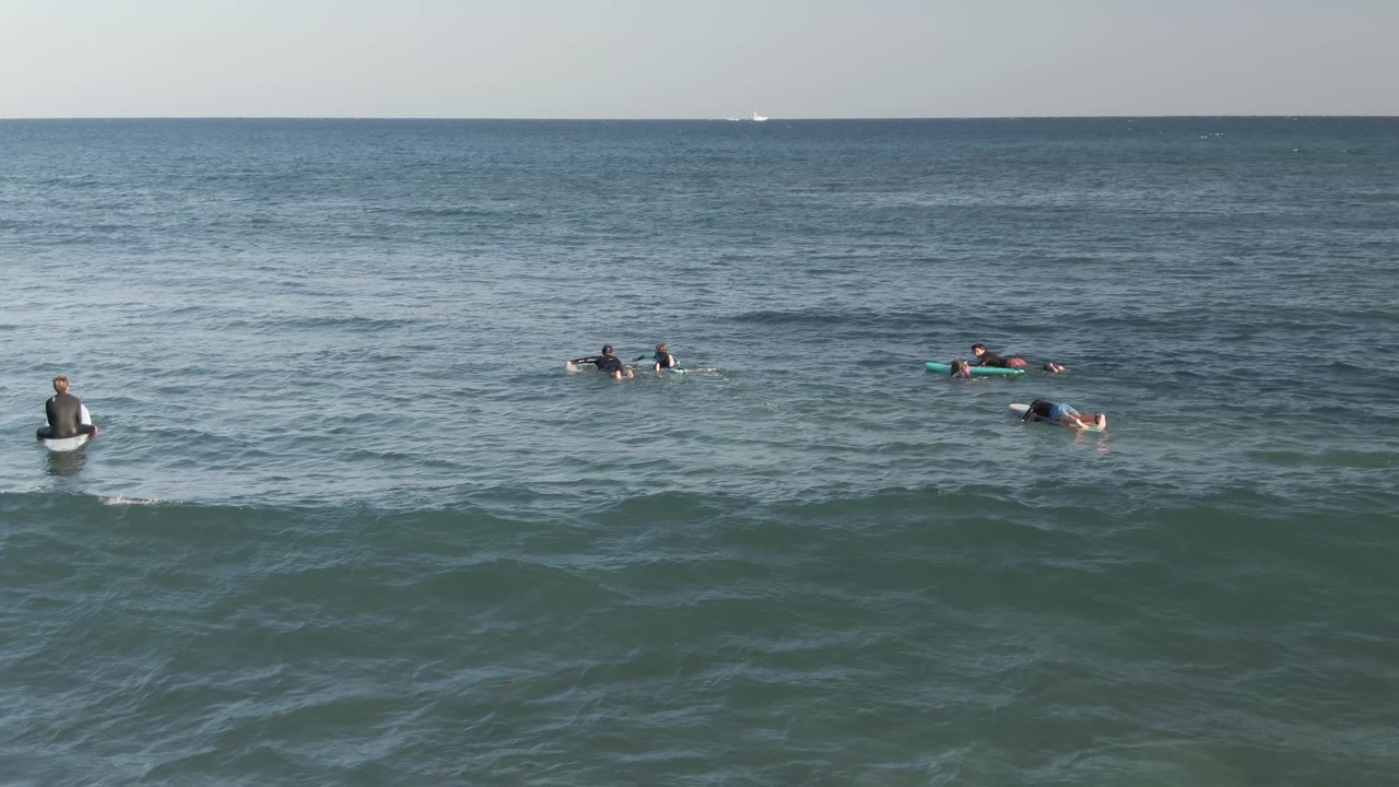 Distant surfers paddling beyond a low ocean swell
