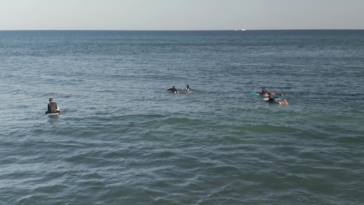 Surfers float on boards in blue-green ocean water at Costa Azul Los Cabos, with a level horizon and small ripples across the foreground.