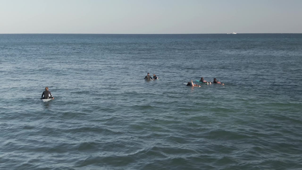 Multiple surfers paddle and wait on boards in blue ocean water.