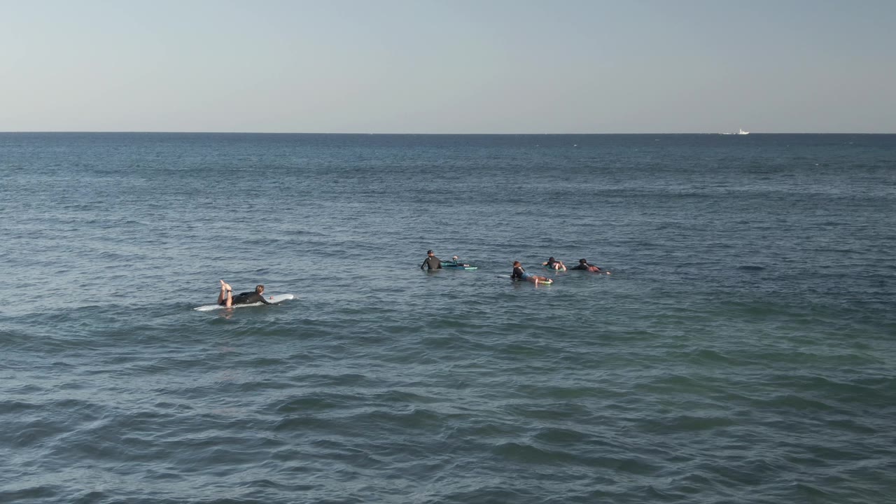 Small groups of surfers waiting on surfboards in open water.