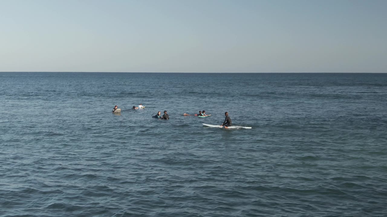 Several surfers and bodyboarders paddling and waiting near the horizon.