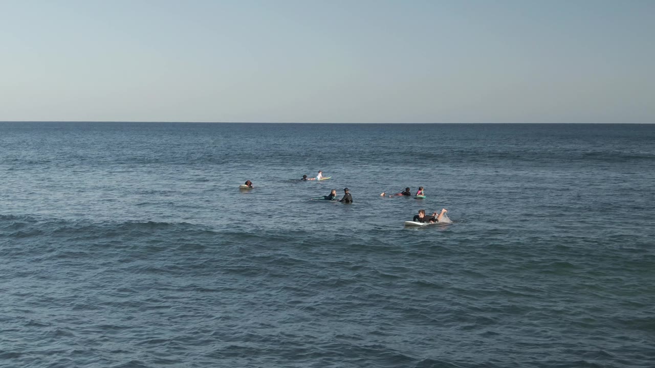 At Costa Azul Los Cabos, distant people float and tread water across a wide blue ocean frame with a steady horizon and pale sky.