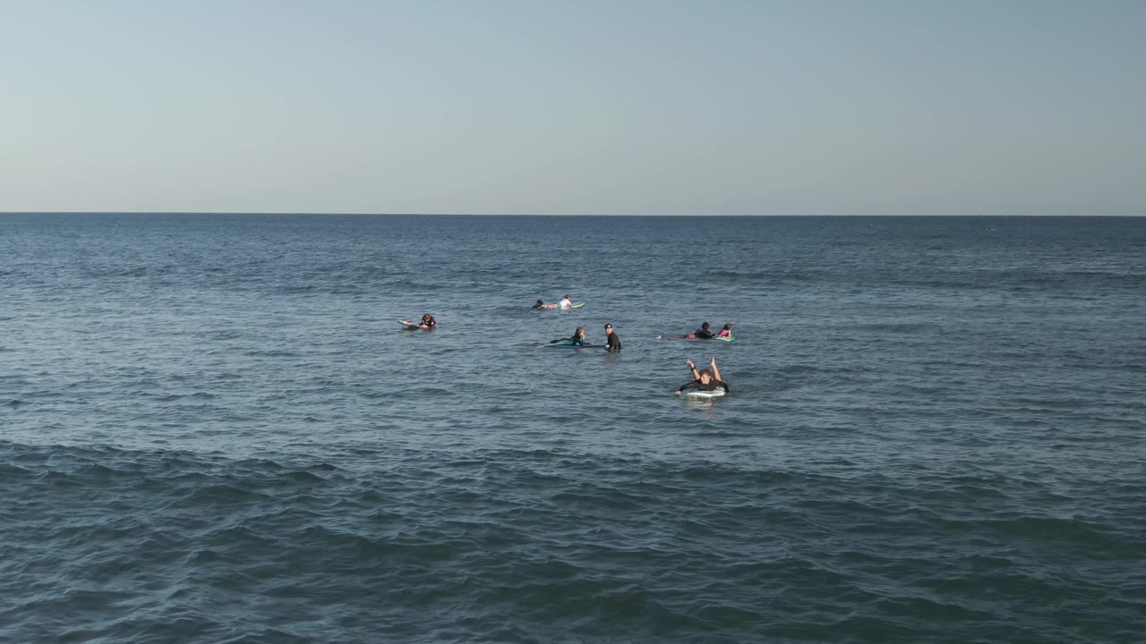 At Costa Azul Los Cabos, small groups of people remain visible beyond darker rolling surface texture in the foreground ocean.