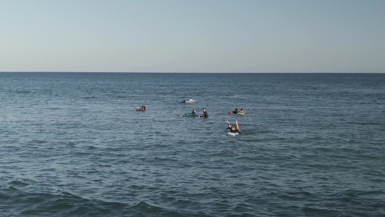 Wide ocean frame with swimmers dispersed near the horizon line.