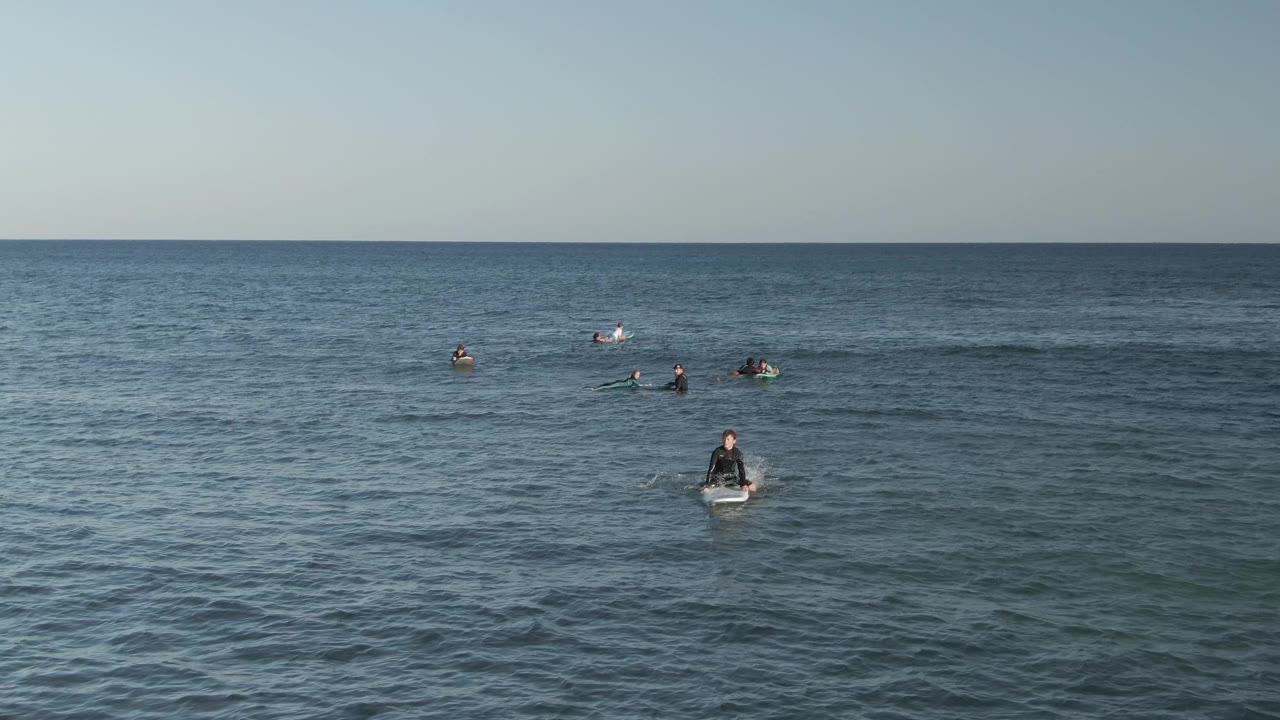 Several surfers wait on boards as a gentle swell crosses the ocean.