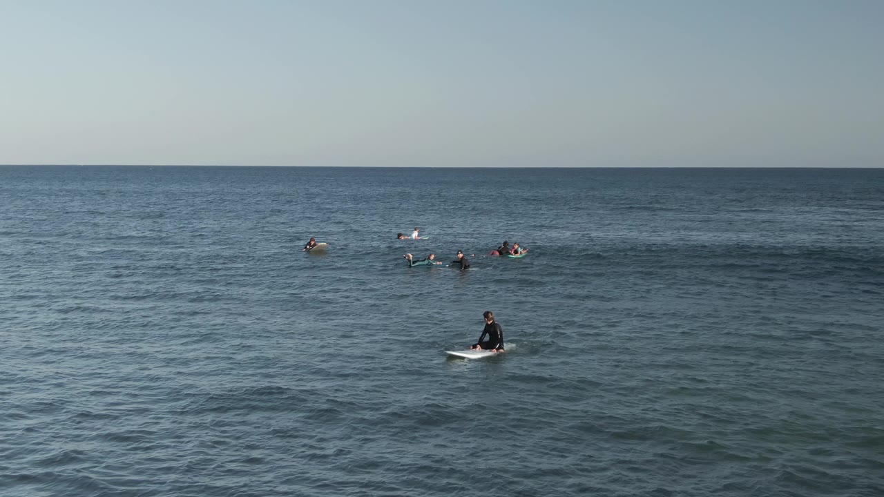 Costa Azul Los Cabos surf lineup with small surfer groups separated across the frame, textured blue-green water below, and open sea behind them.