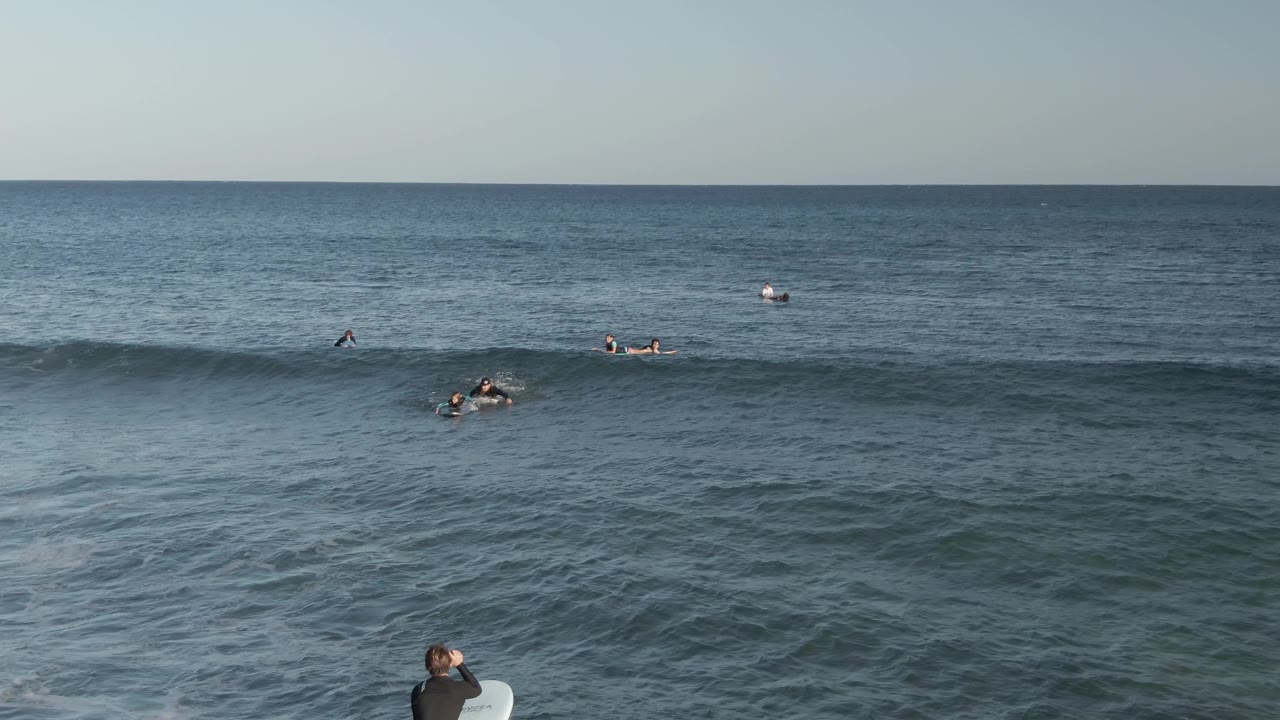 Surfers paddle as a small wave rises across the ocean