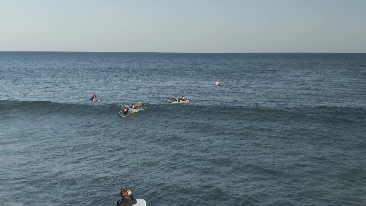 A rolling wave crosses the middle of the Costa Azul Los Cabos ocean view while multiple surfers remain spaced out behind it.