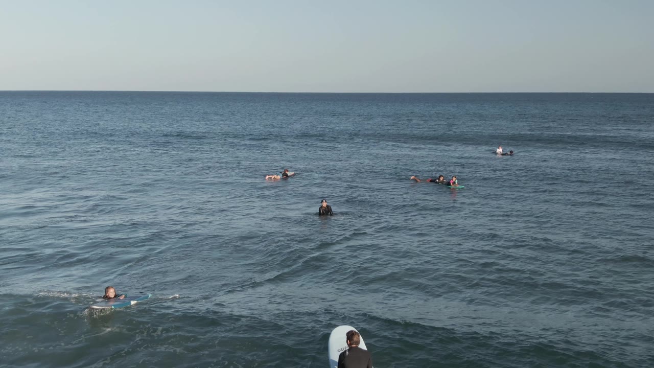 Surfers wait and paddle in blue water under a low sky.