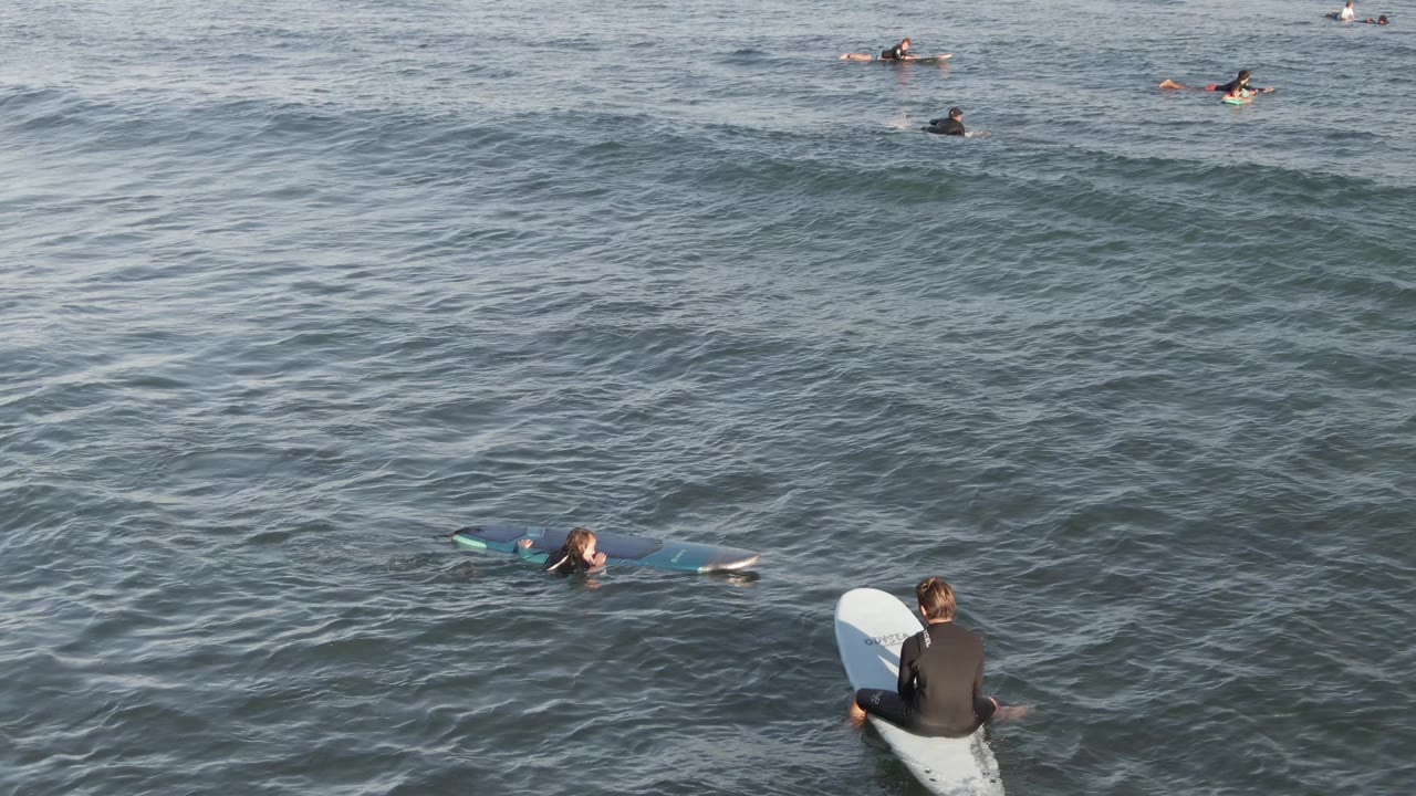 Surfers spaced across open ocean with small waves.