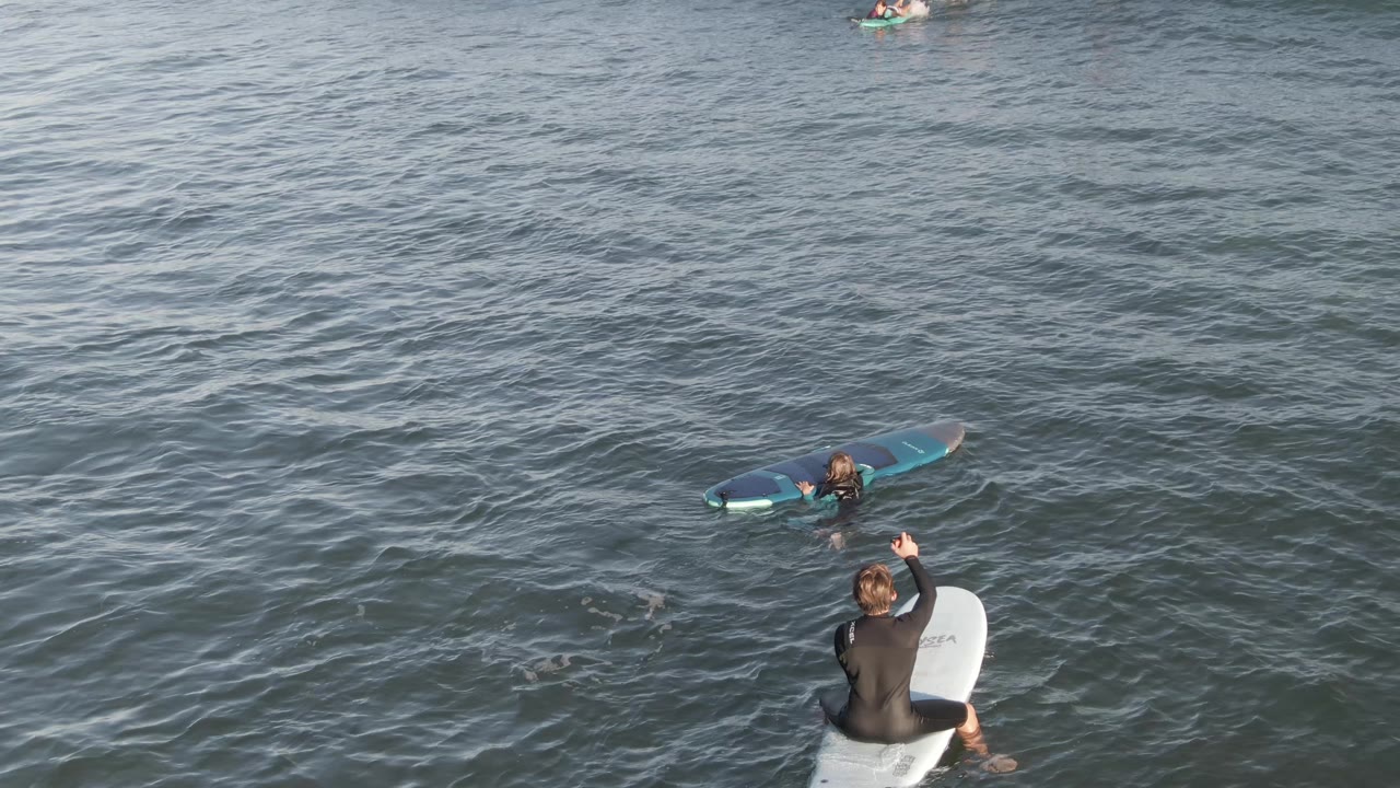 Foreground surfer raises an arm while another surfer floats nearby.