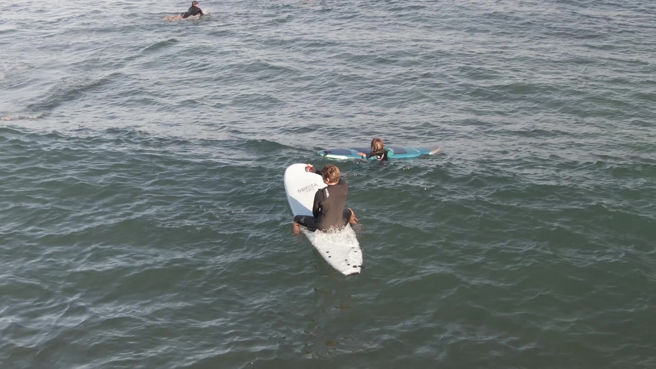 Surfers paddle and wait among small ocean swells.