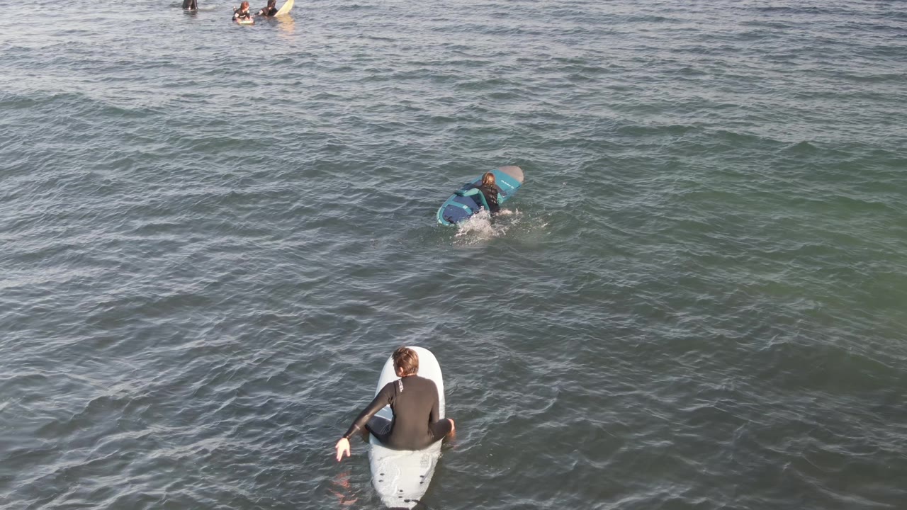 Aerial view in Costa Azul Los Cabos with the foreground surfer slightly right of center on a white board and another surfer paddling near a small breaking ripple.