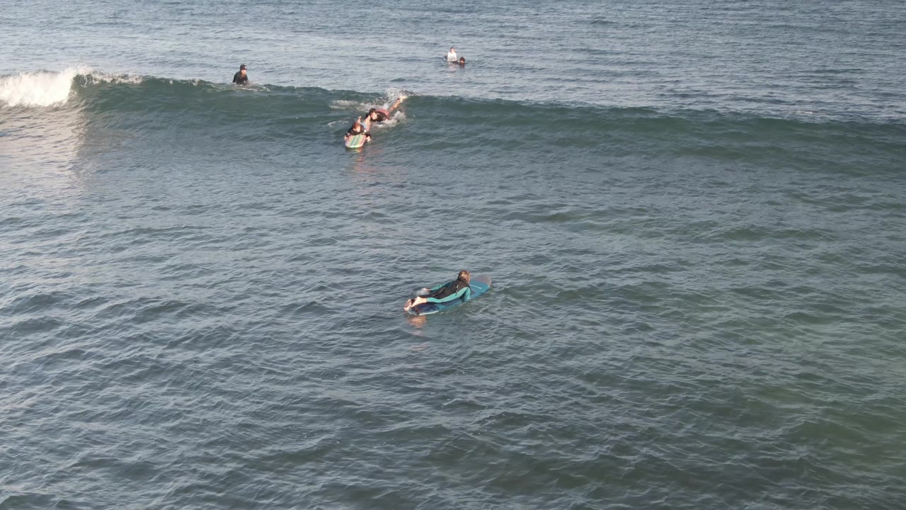 At Costa Azul Los Cabos, several surfers and bodyboarders are spread across green-blue water while a wave starts to lift near the top of the frame.