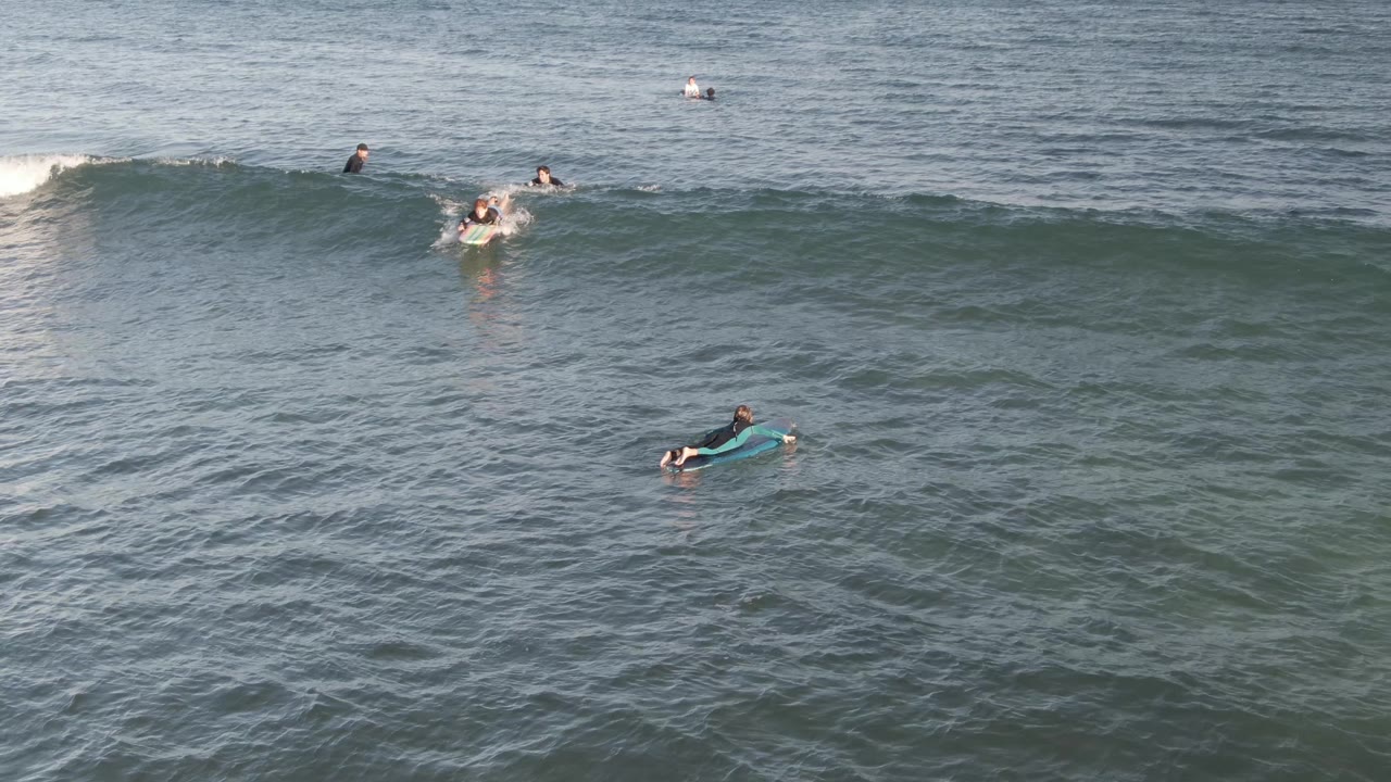A surfer paddles into a forming wave while other riders wait nearby.