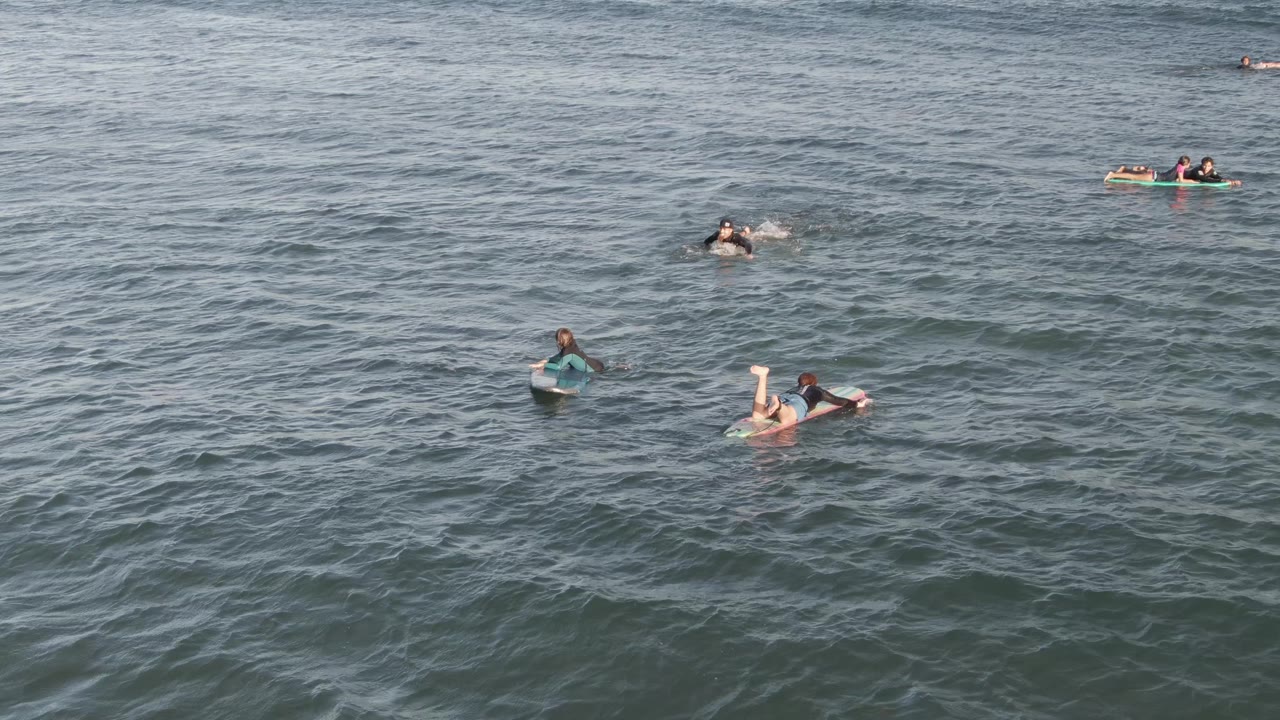 Aerial view at Costa Azul Los Cabos of several people spread across blue-green ocean water, with one person on a board at left and others floating farther out.