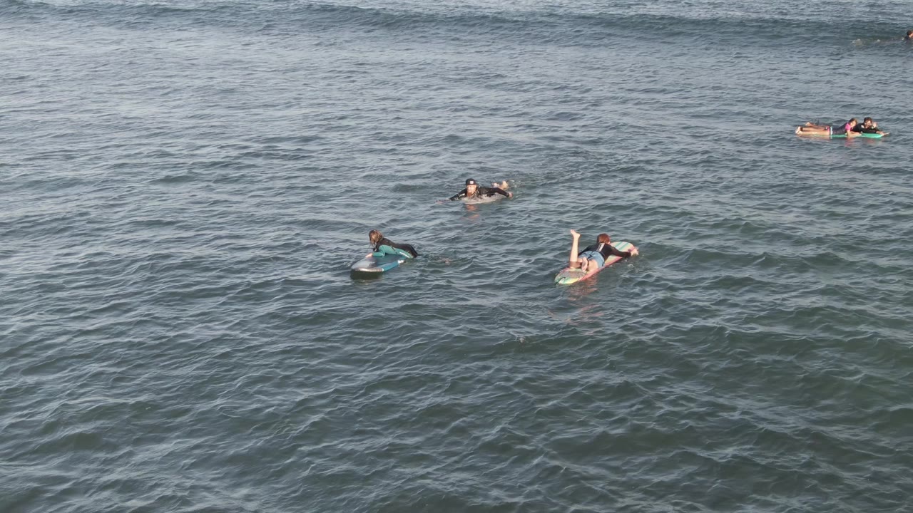 Costa Azul Los Cabos ocean view with several people dispersed across the frame, including two floaters near the right and darker swimmers farther back in the water.